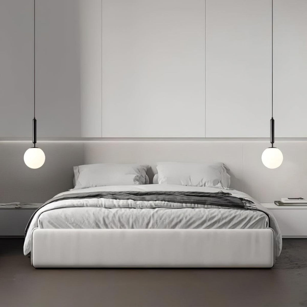 Two black-and-white Clérachic sphere pendants flank a bed against a panelled grey wall.