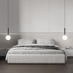 Two black-and-white Clérachic sphere pendants flank a bed against a panelled grey wall.