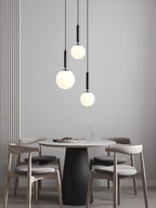 Three black-and-white Clérachic sphere pendants hang at staggered heights above a round dining table.