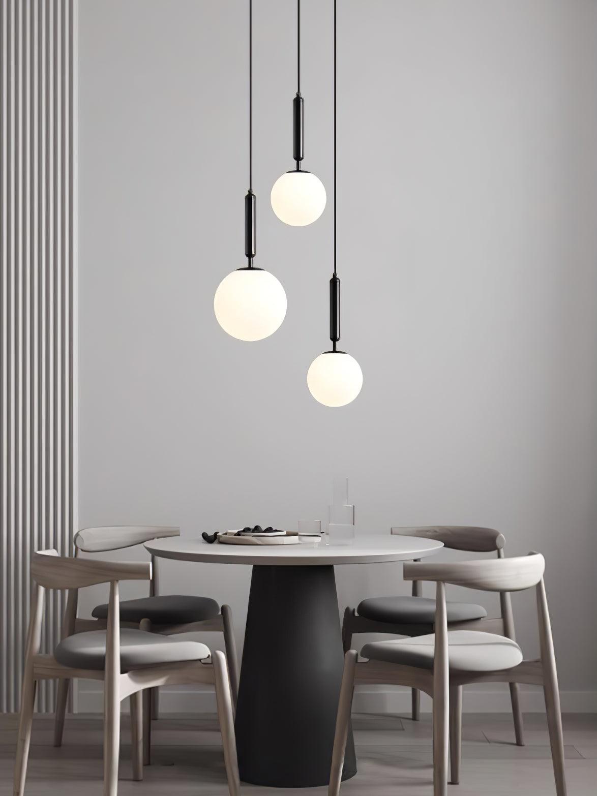 Three black-and-white Clérachic sphere pendants hang at staggered heights above a round dining table.