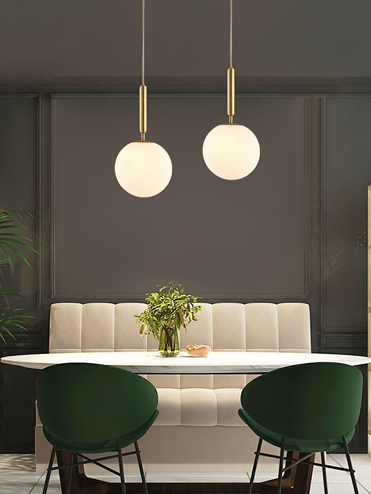 Green velvet chairs sit beneath two brass-and-white Clérachic sphere pendants in this dining scene.