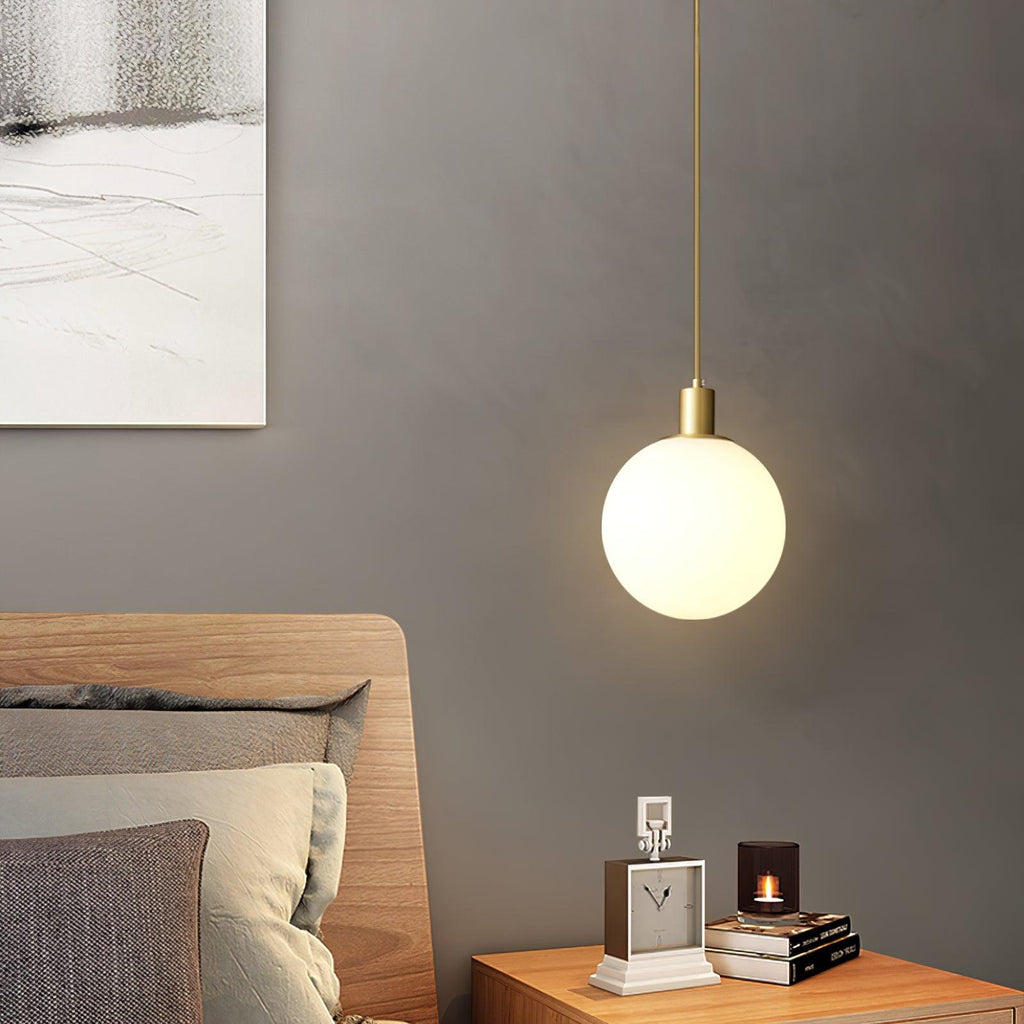 A single brass-and-white Clérachic sphere pendant hangs beside a bed with a clock and candle on the nightstand.