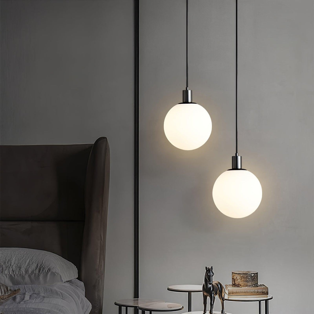 Two black-and-white Clérachic sphere pendants hang at different heights in a grey bedroom.