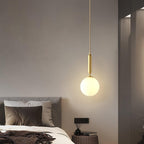 A single Clérachic sphere pendant glows brass and white against a plain grey bedroom wall.