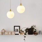 A shelf of wood letter blocks sits beneath two brass-and-white Clérachic sphere pendants at staggered heights.