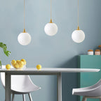 Lemons sit on a table beneath three brass-and-white Clérachic sphere pendants against a teal wall.