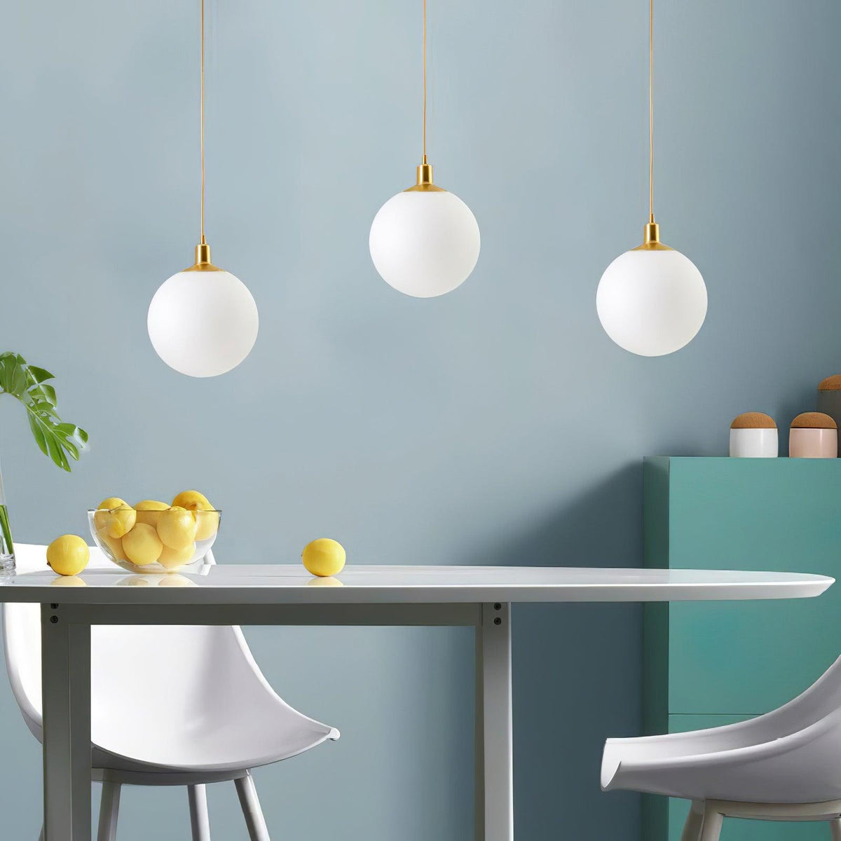Lemons sit on a table beneath three brass-and-white Clérachic sphere pendants against a teal wall.