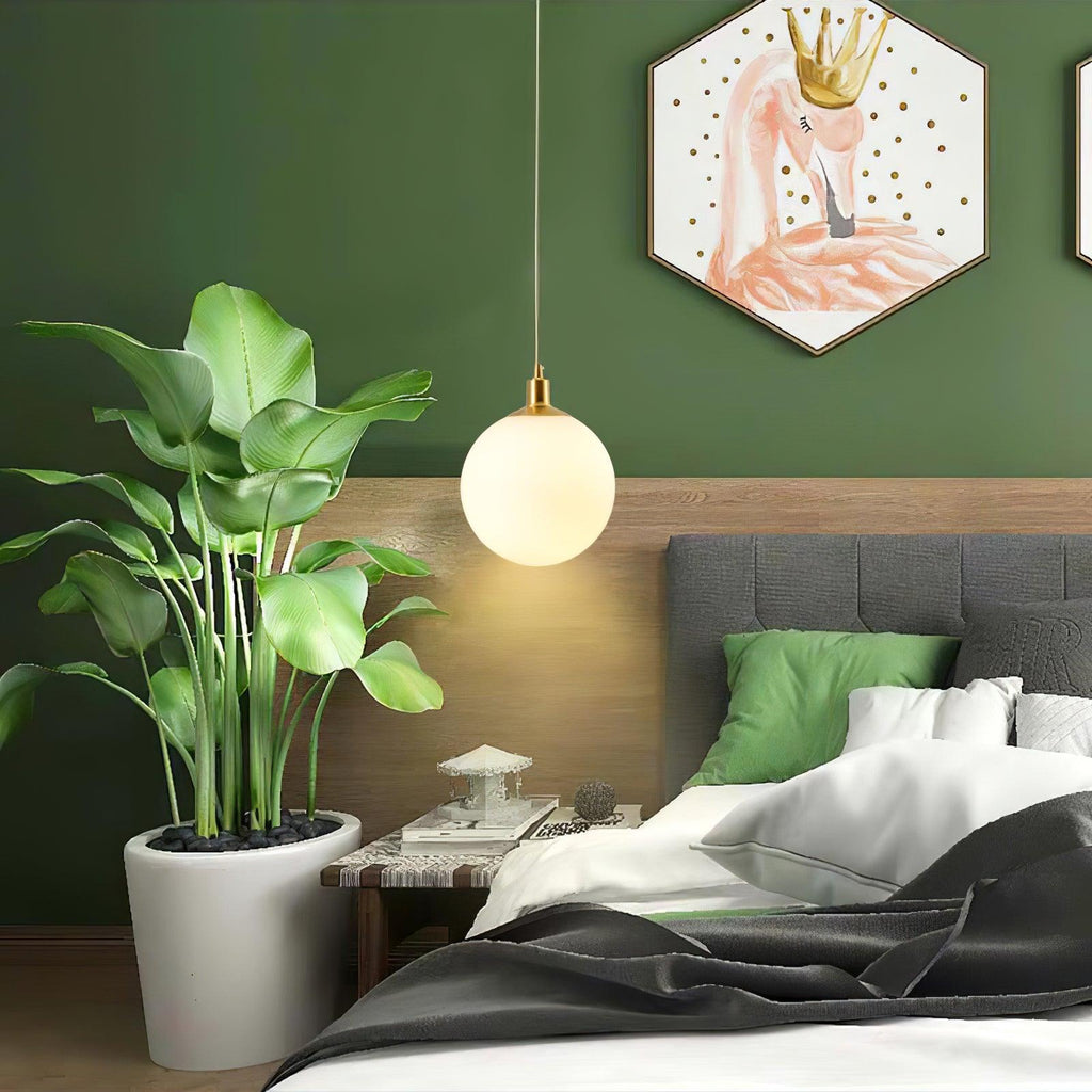 A single brass-and-white Clérachic sphere pendant hangs beside a plant in a green bedroom.