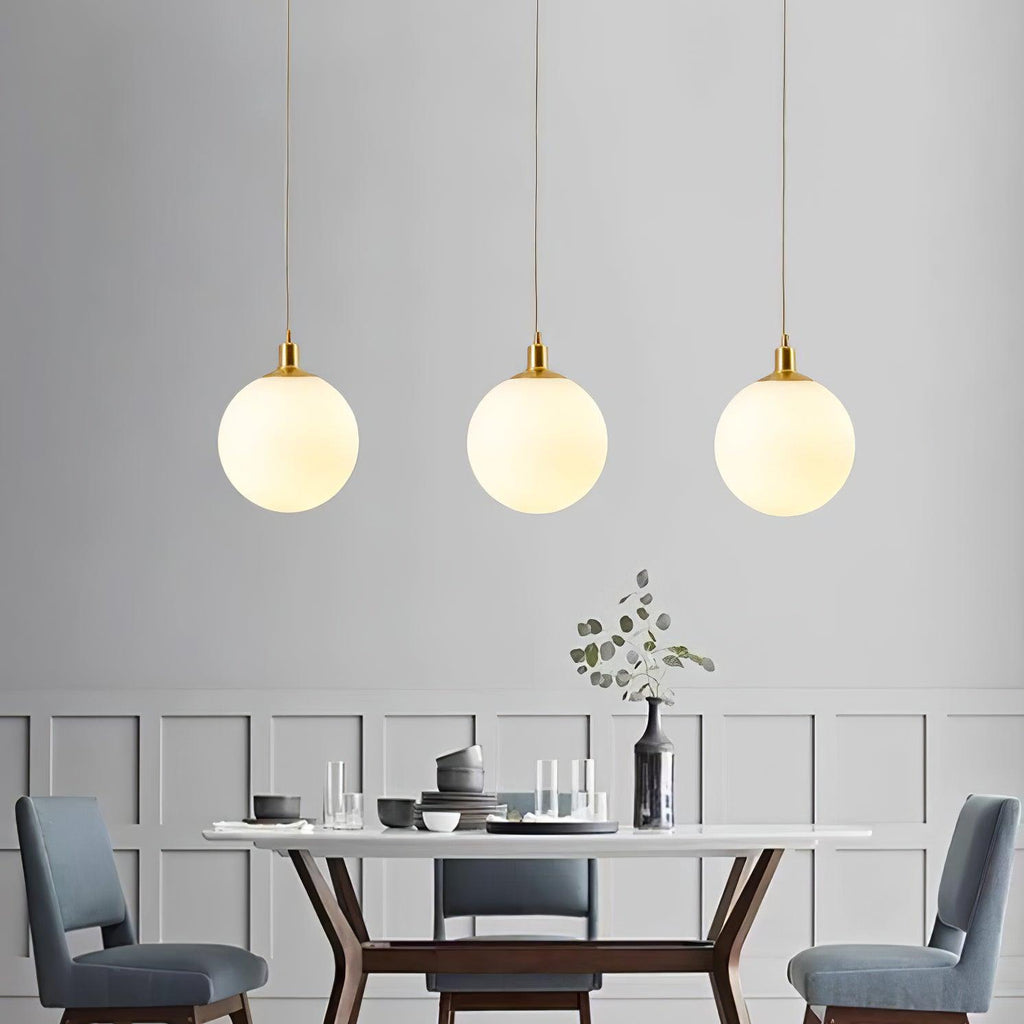 Blue upholstered chairs sit beneath three brass-and-white Clérachic sphere pendants in this dining room.