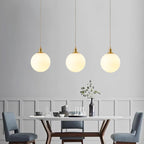 Blue upholstered chairs sit beneath three brass-and-white Clérachic sphere pendants in this dining room.