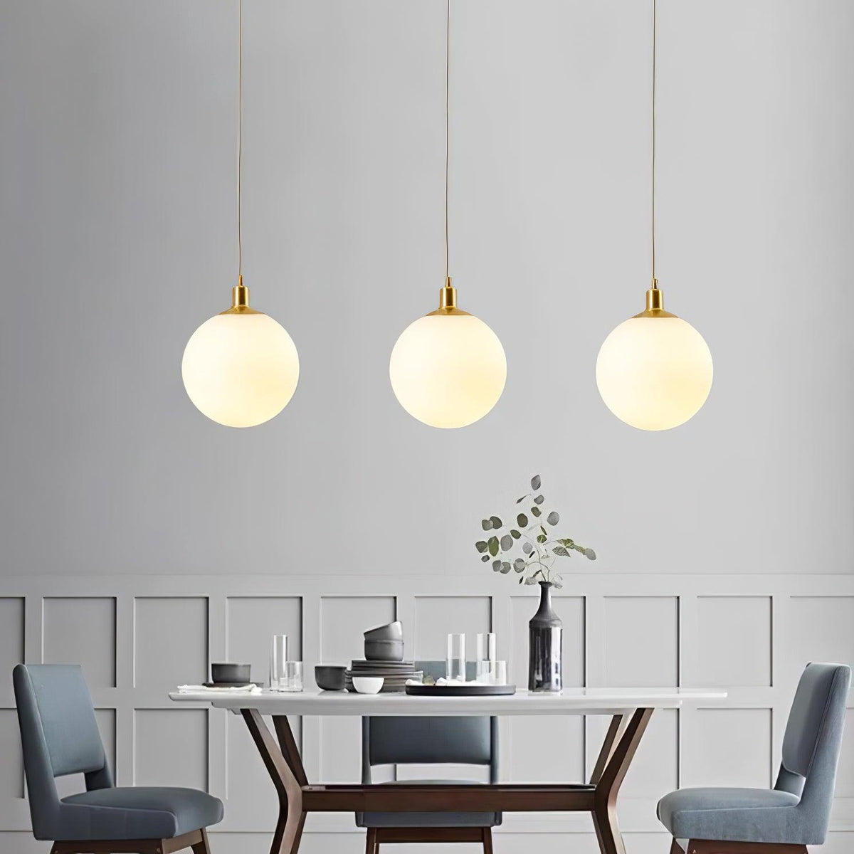 Blue upholstered chairs sit beneath three brass-and-white Clérachic sphere pendants in this dining room.