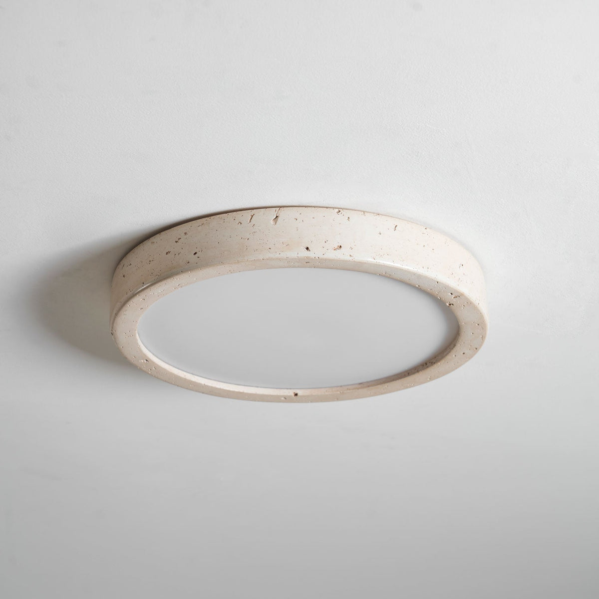 This Clérachic ceiling light is shown unlit, tilted to reveal the depth of its travertine ring against plain grey.