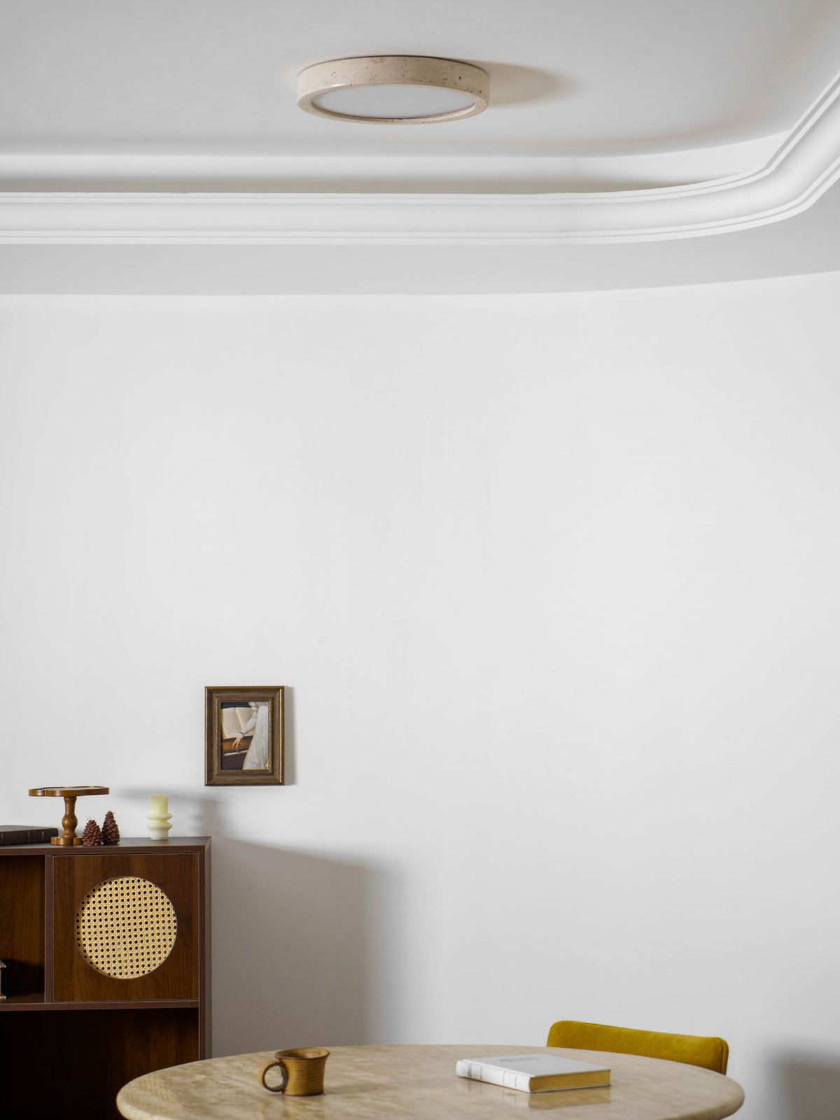 Unlit in the corner of a room with cornice moulding, this Clérachic ceiling light sits above a cane cabinet and a set table.