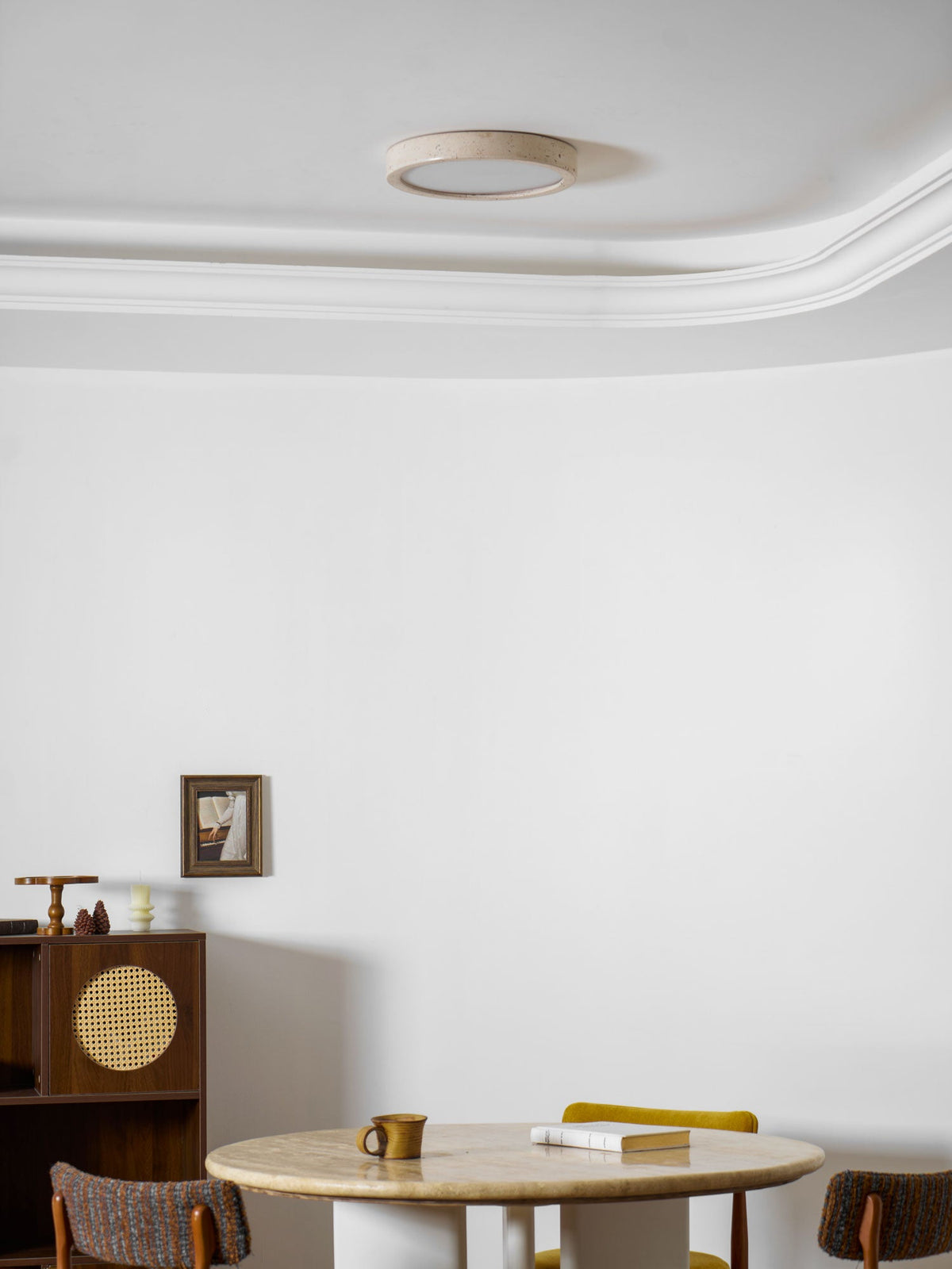 Seen close to the cornice, this Clérachic ceiling light is unlit above the cane cabinet and round travertine table.