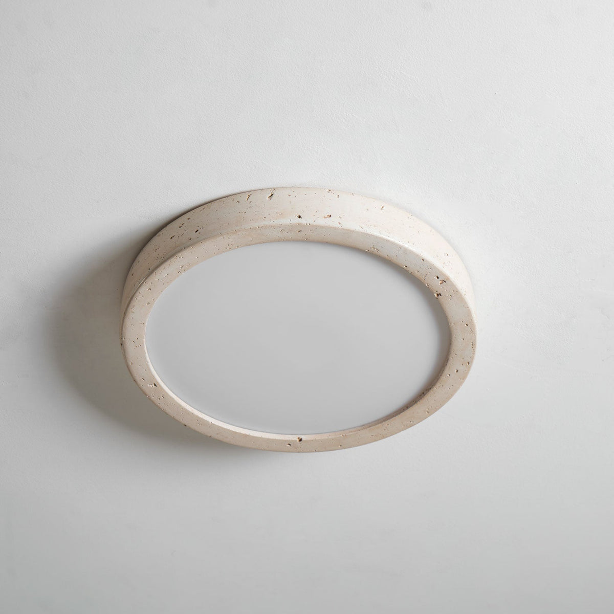 A different angle shows this Clérachic ceiling light unlit, its travertine ring edge lit by soft studio light against grey.