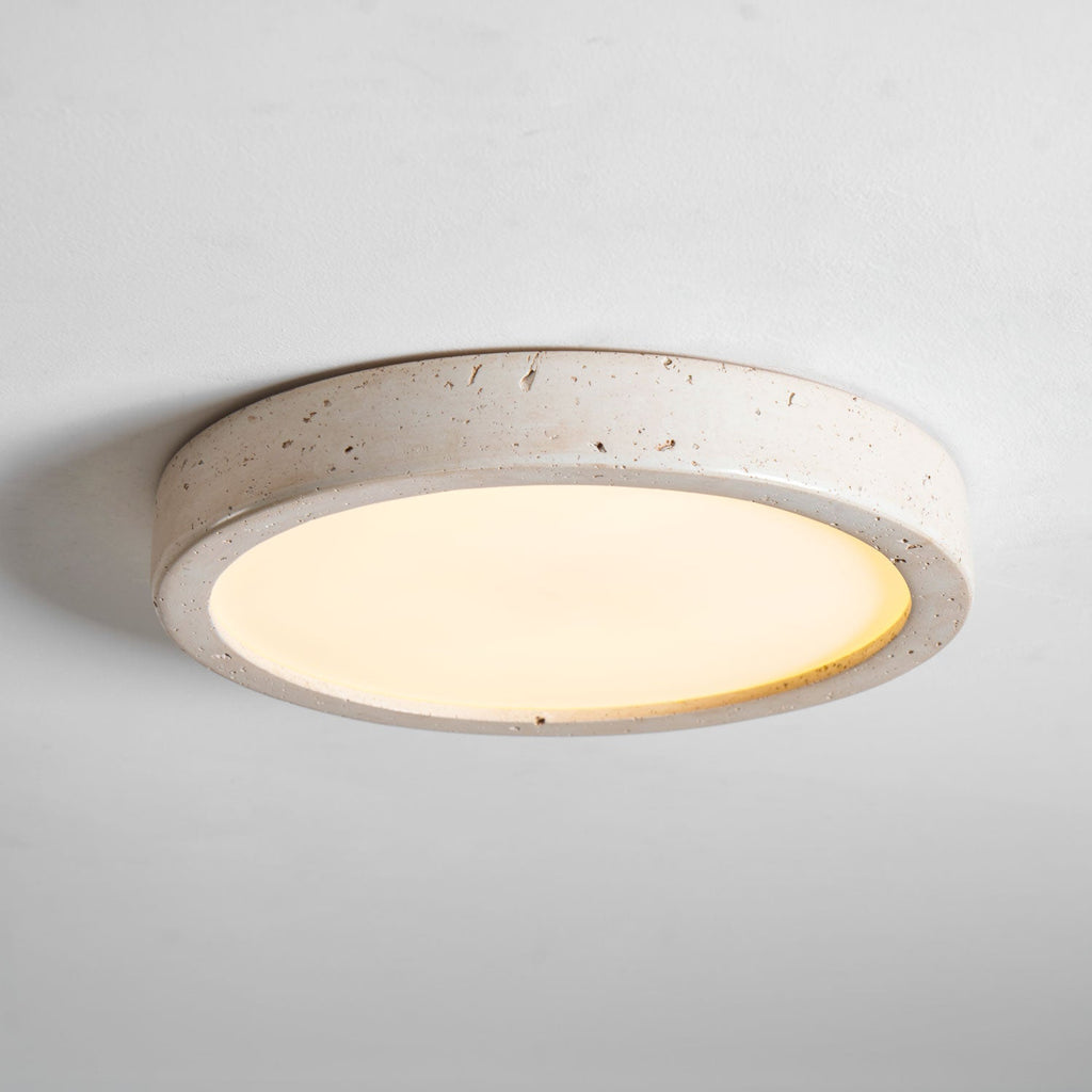 Photographed unlit from a low angle, this Clérachic ceiling light's travertine ring stands out against a plain grey background.