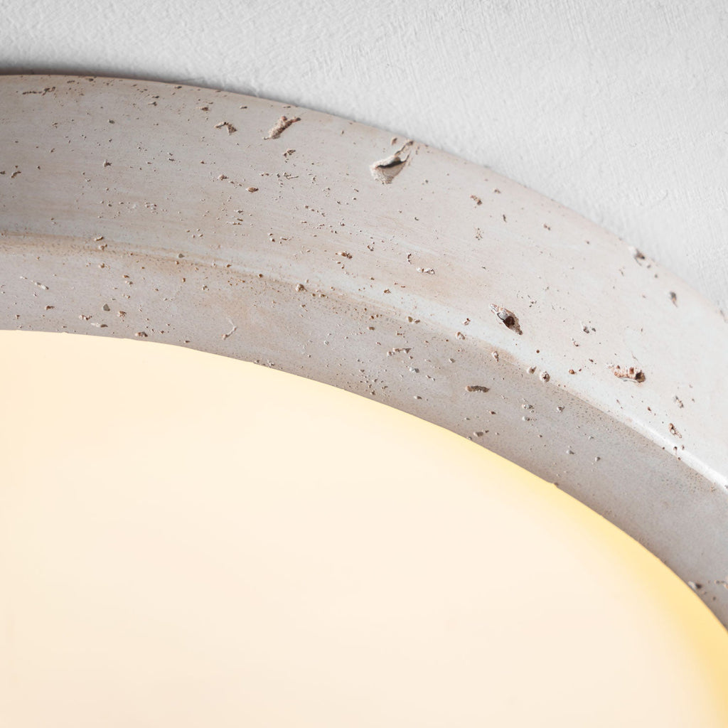 Close view of the travertine ring on this Clérachic ceiling light, lit warmly to show its natural veining and pitting.