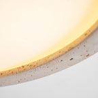 Extreme close-up of the travertine ring on this Clérachic ceiling light, lit warmly to show the stone's texture.