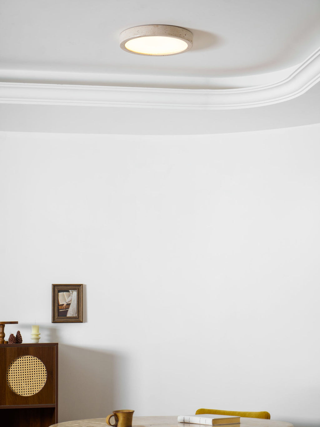 Glowing warmly near a decorative cornice, this Clérachic ceiling light lights a room with a cane-front cabinet and a round table.