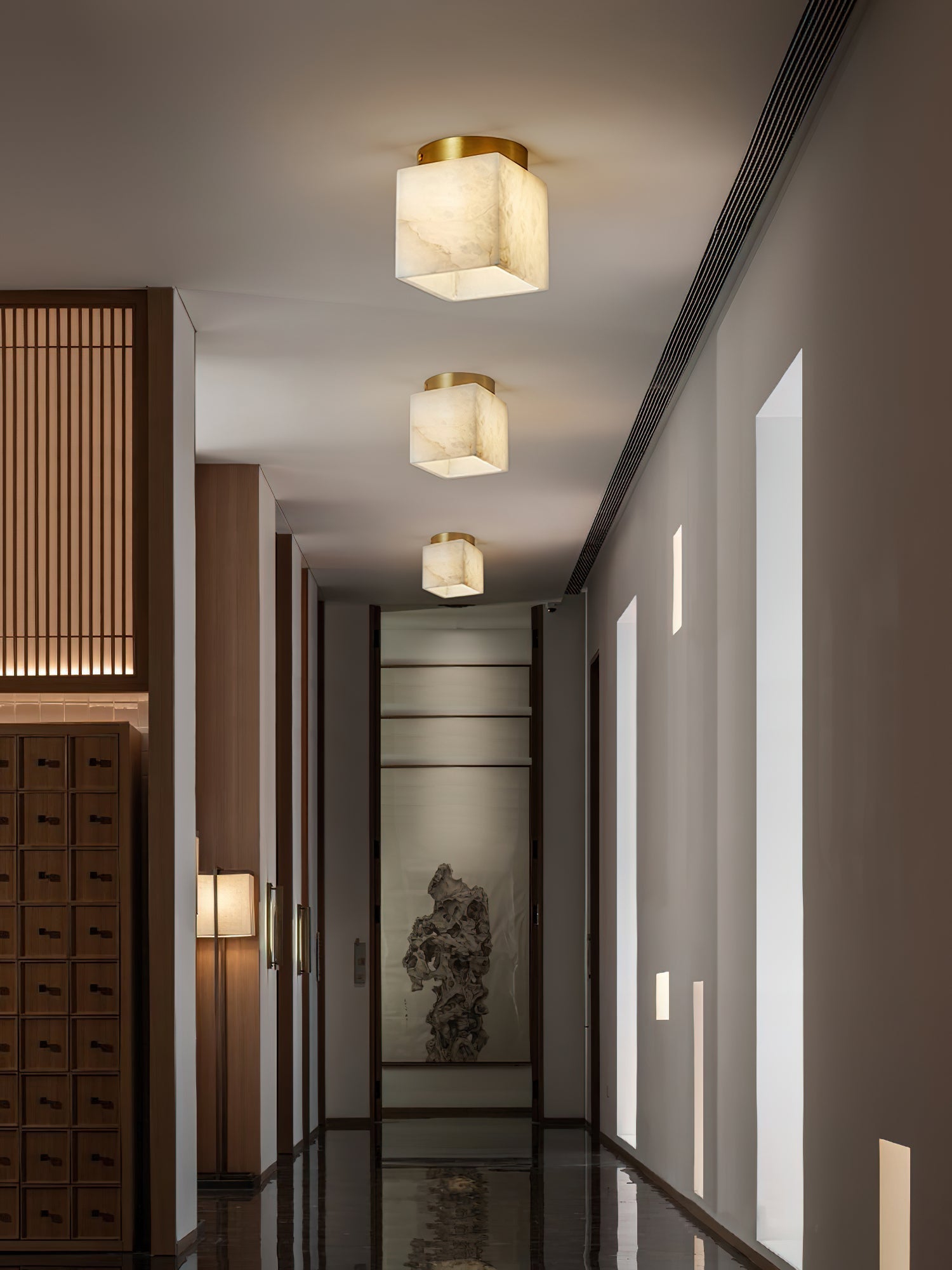 Three Usilia alabaster ceiling lights lit down a long corridor with wood cabinetry and recessed wall slots.