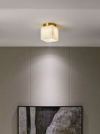 Usilia alabaster ceiling light lit above a linen-panelled wall, casting a soft pool of light down the wall.