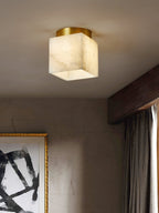 Usilia alabaster ceiling light lit close to camera in a plaster-walled room with a dark timber beam and curtain.