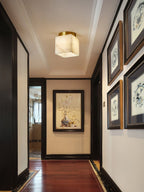 Usilia alabaster ceiling light lit in a narrow corridor lined with framed prints and dark wood trim.