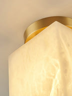Detail of the round brass canopy from below, with the pointed corner of the lit alabaster shade against it.