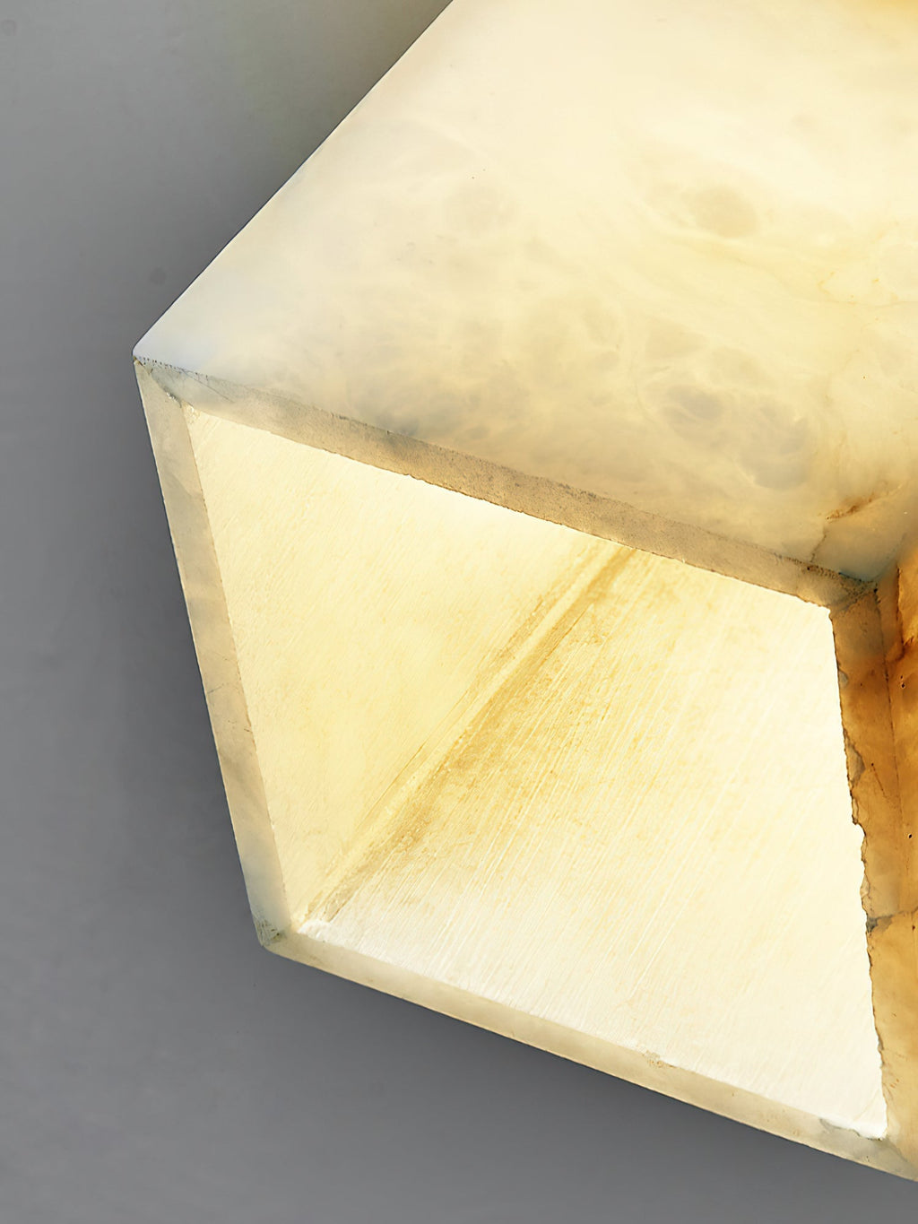 Close crop of the open underside of the alabaster shade, lit from within so the cut stone edges glow warm.