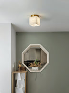 Usilia alabaster ceiling light lit beside a sage green wall with an octagonal mirror and wooden console below.