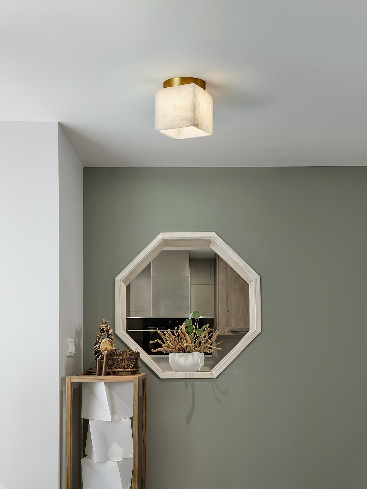 Usilia alabaster ceiling light lit beside a sage green wall with an octagonal mirror and wooden console below.