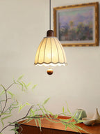 Close beside a framed painting, this Clérachic pendant's fluted beige shade hangs above trailing greenery.
