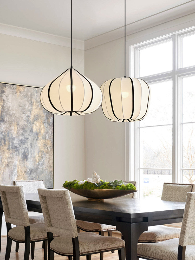 Two Clérachic pendants, one tapering and one rounded, glow warm above a dark dining table set near a tall window.