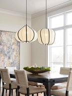 Two Clérachic pendants, one tapering and one rounded, glow warm above a dark dining table set near a tall window.