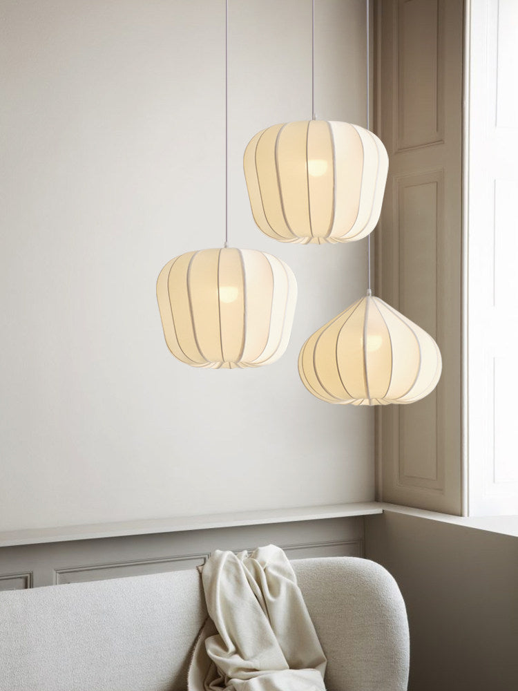 Three Clérachic pendants glow warm at staggered heights in a room corner with an upholstered sofa and folded throw.