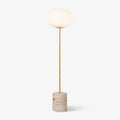 A Clérachic floor lamp with a frosted glass globe and slim brass stem on a rounded travertine base, shot on white.