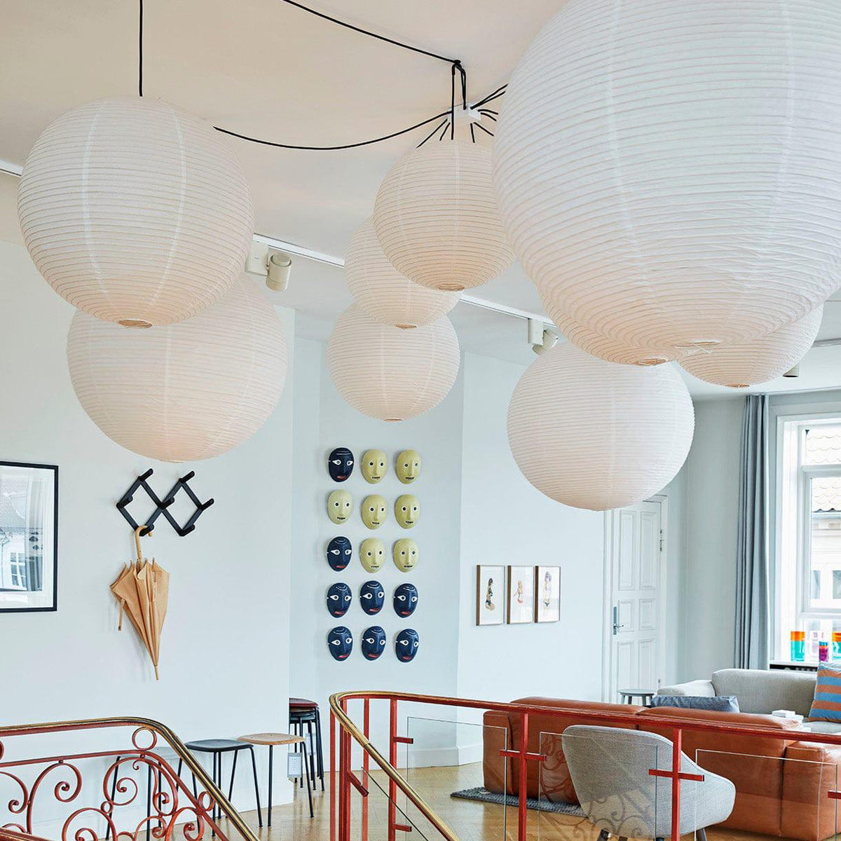 Several globe pendants from Clérachic cluster near a stairwell hung with small framed prints and a red iron railing.