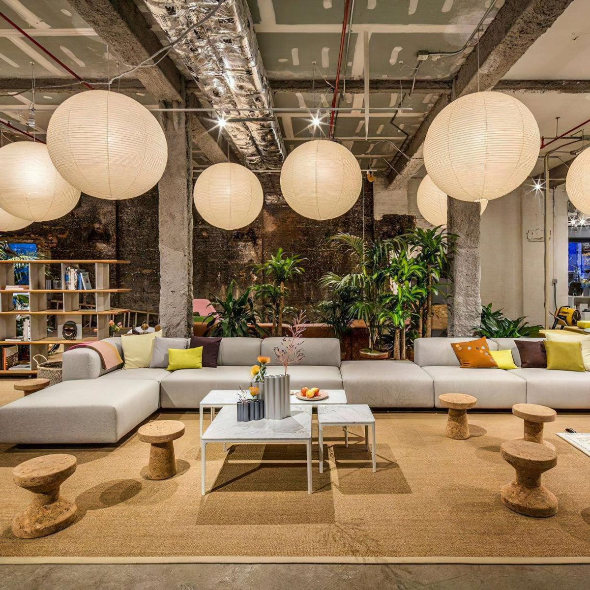 Several lit mulberry paper globes from Clérachic hang together in an industrial loft with exposed pipes and low stools.