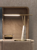 Clérachic gold table lamp with a slender LED bar over a solid white marble cone base, lit on a beige dresser in front of a mirrored panel.