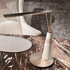Close-up of the Clérachic table lamp's marble cone base and bronze-finish LED bar, set unlit on a dark brown marble tabletop.