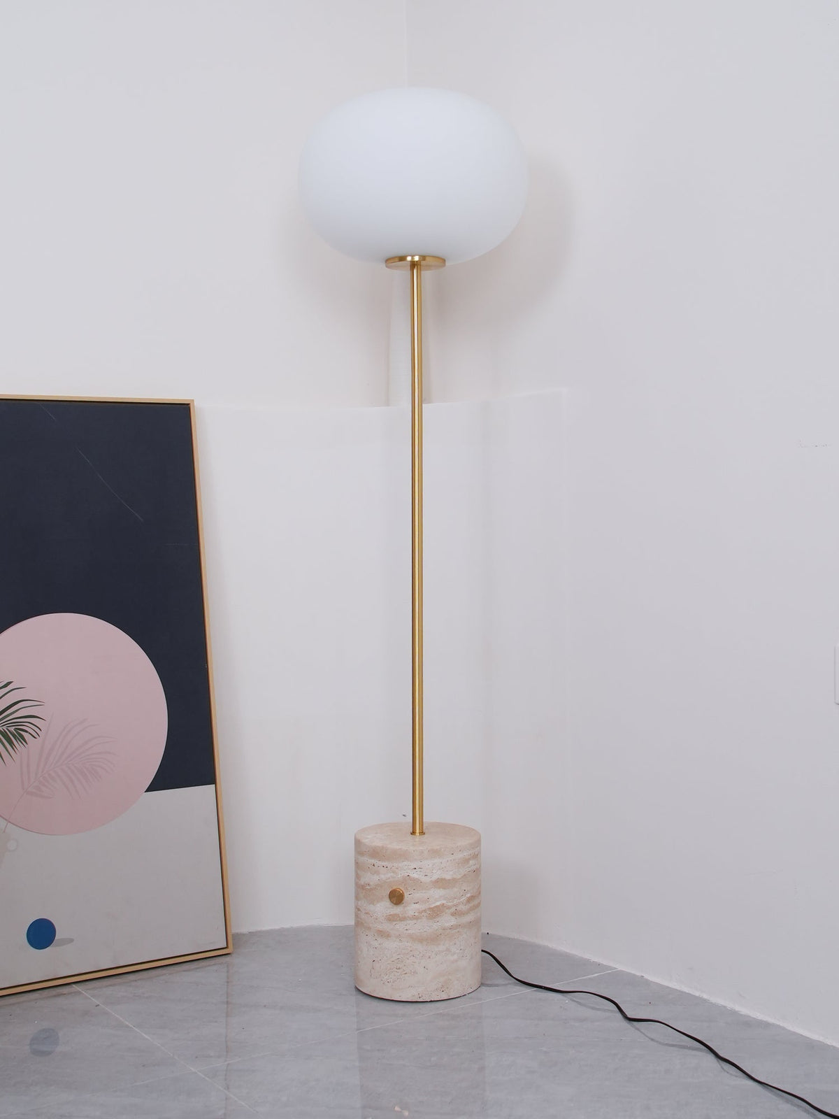The Clérachic floor lamp stands in a white corner, its frosted globe pale against the abstract print leaning behind it.