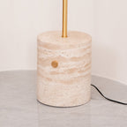 Close-up of the Clérachic floor lamp's travertine base, showing its veined stone, brass push-button switch and cord.