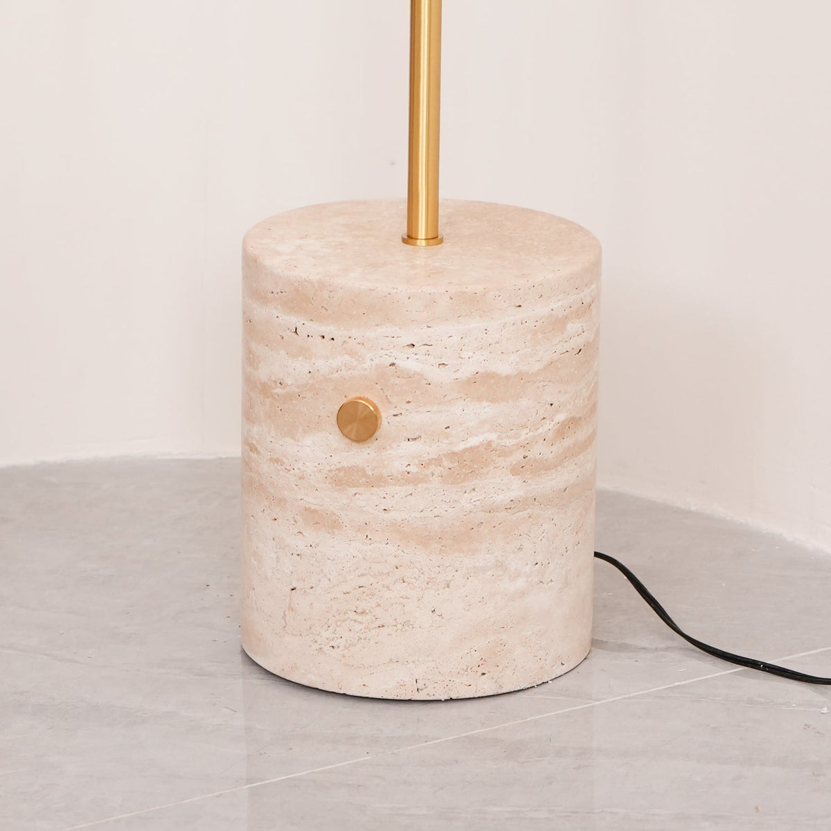 Close-up of the Clérachic floor lamp's travertine base, showing its veined stone, brass push-button switch and cord.
