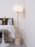 The Clérachic floor lamp stands near a fringed white tablecloth set with fresh flowers and magazines, on a tiled floor.