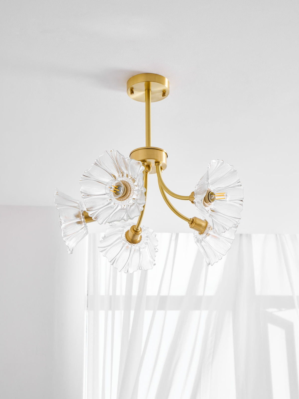A wider view shows this Clérachic chandelier beside a sunlit sheer curtain, its glass petal shades spread outward.