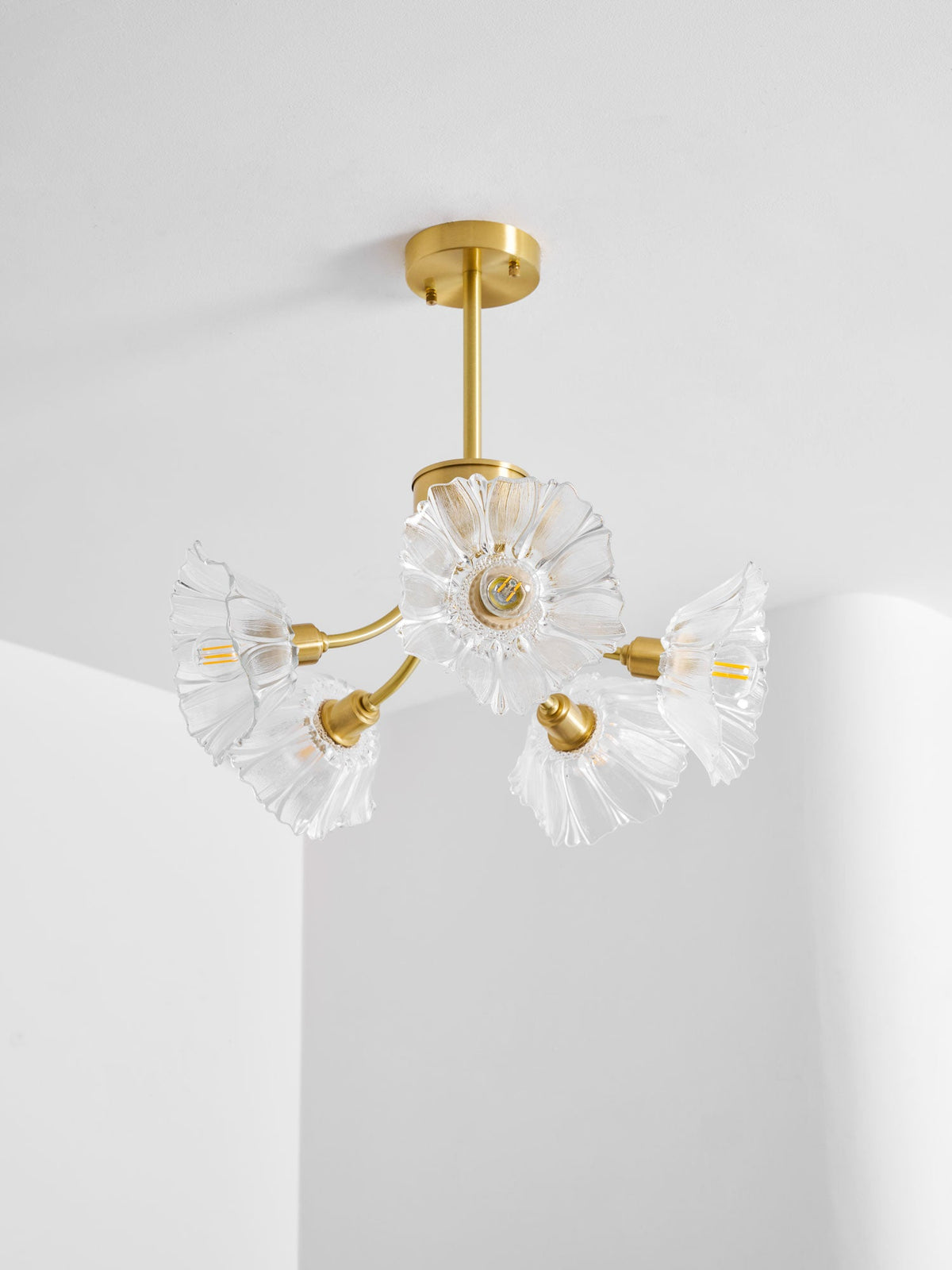 Ruffled glass shades sit close together on this Clérachic chandelier, hung in a corner near a sheer curtain.