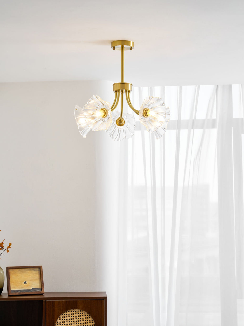 Another view beside a sheer curtain shows this Clérachic chandelier's brass arms spread with ruffled glass shades.