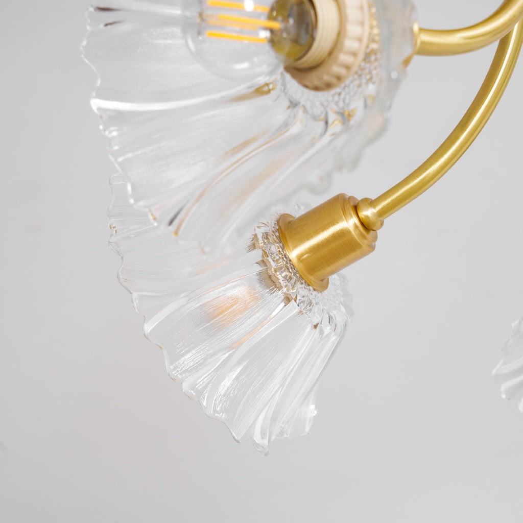 Close-up of the brass socket and ruffled glass shade on this Clérachic chandelier, the bulb's filament visible inside.
