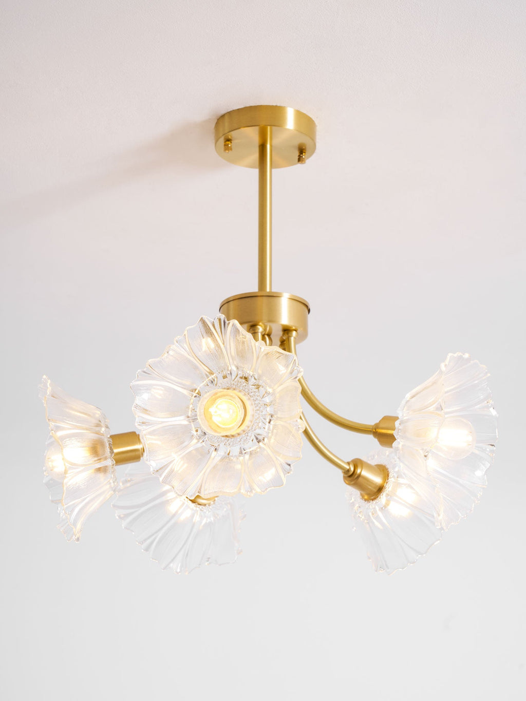 A closer angle shows the brass ceiling mount of this Clérachic chandelier, with glass petal shades fanning outward against a white backdrop.