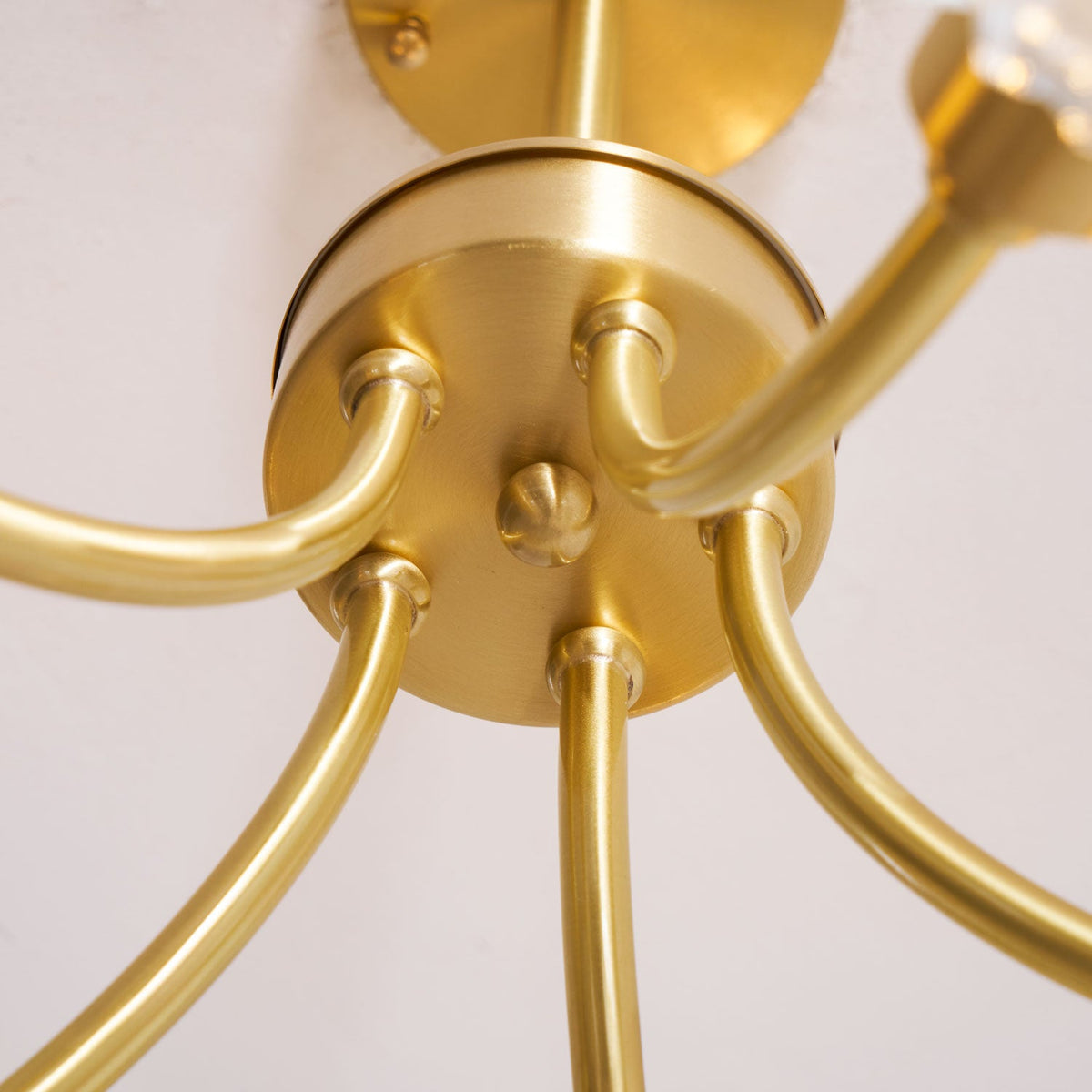 Close-up of the brass ceiling mount on this Clérachic chandelier, showing where its multiple arms converge.
